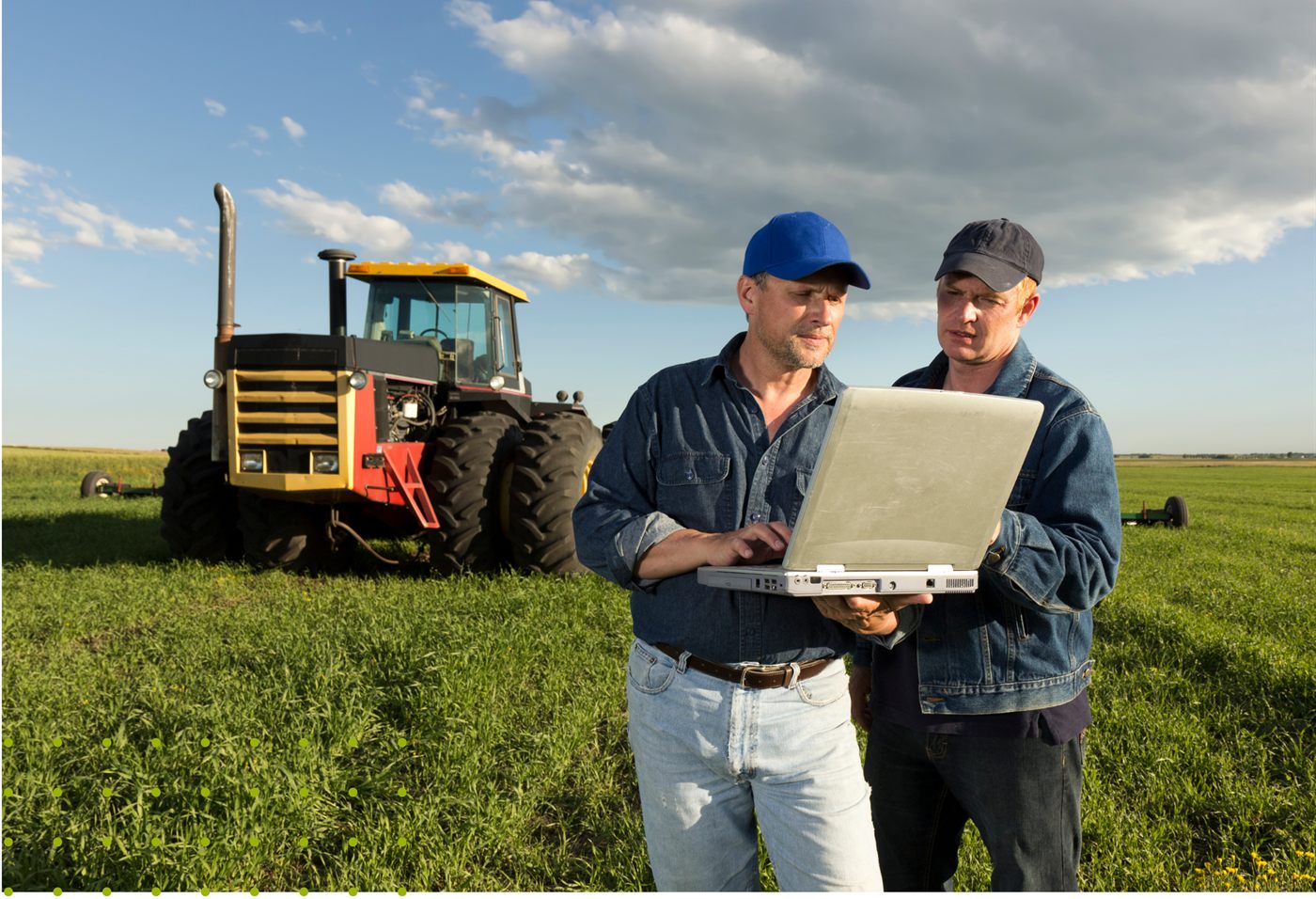 Dois técnicos analisando dados em um notebook ao lado de um trator no campo